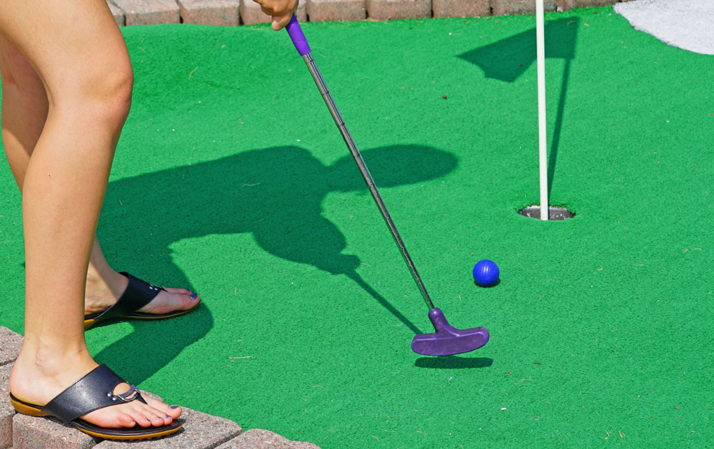 Person putting blue ball on mini golf green
