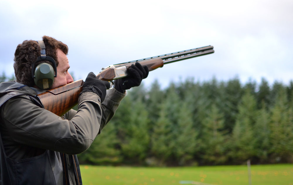 Man aiming shotgun at clay pigeon shooting range